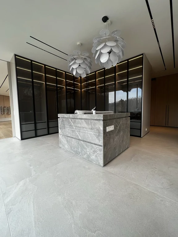 Centralny punkt garderoby: monolityczna wyspa z kamiennym wykończeniem i gniazdami w boku. W tle witryny i oświetlenie dekoracyjne.