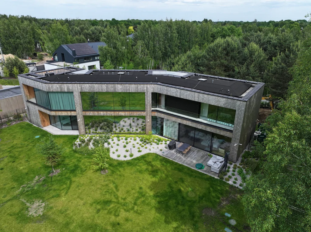 Dom Prawdziwka – ujęcie z drona z ukosa: duże przeszklenia, taras i zieleń wokół budynku.