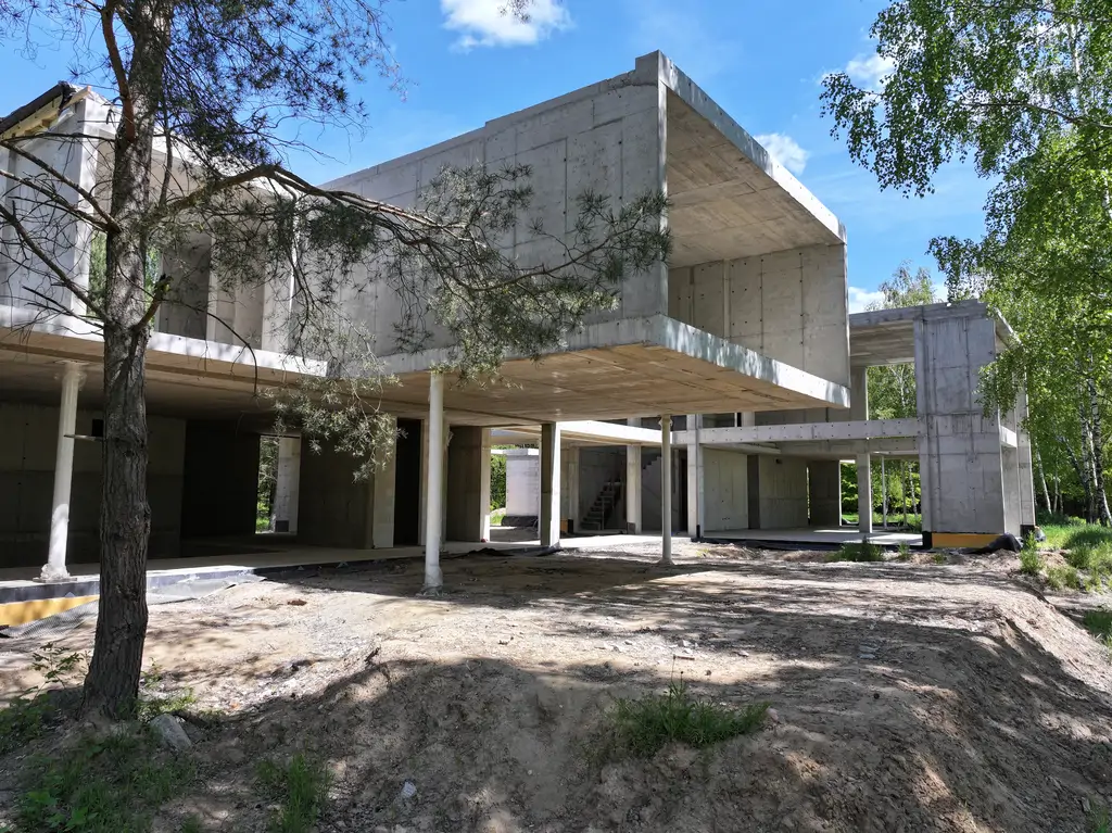 Nowoczesny dom z betonu architektonicznego w trakcie budowy – widok elewacji i bryły od strony ogrodu.