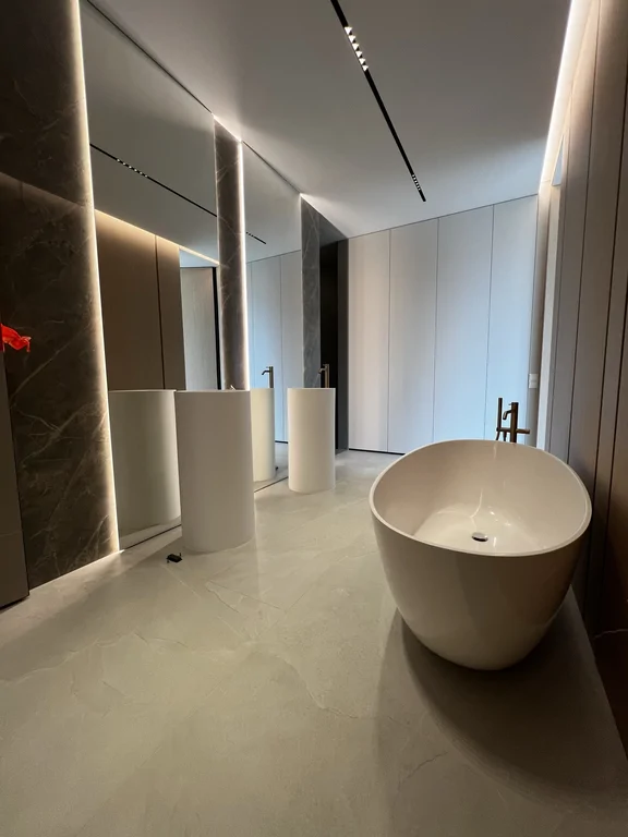 Ujęcie podkreślające głębię wnętrza, liniowe oświetlenie oraz spokojną paletę materiałów: jasna posadzka + ciepłe okładziny.