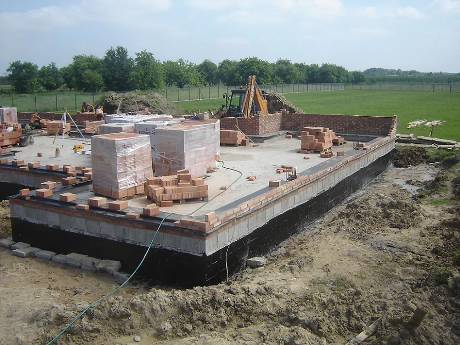 Budowa domu w stanie surowym, wylane ławy fundamentowe, murowanie ścian w tle koparka