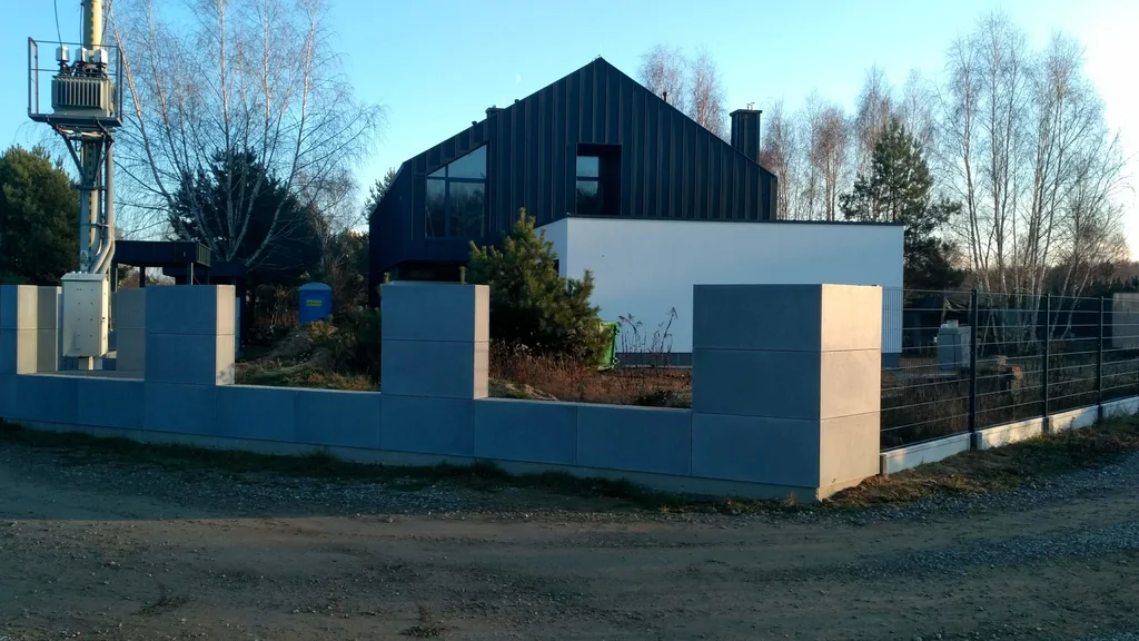 Nowoczesny dom jednorodzinny za betonowym ogrodzeniem, widok od ulicy