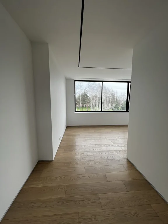 Widok z korytarza na jasny pokój: białe ściany, dębowa podłoga i czarne ramy okienne.