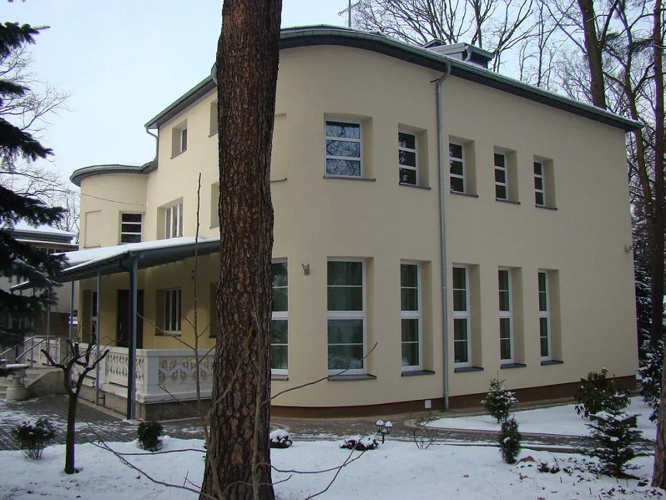 Elewacja boczna budynku po remoncie; długi rząd wysokich okien, zima i śnieg na terenie