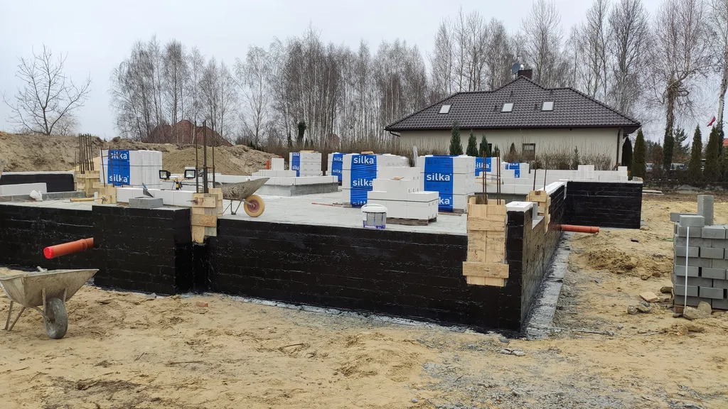 Hydroizolacja pionowa ścian fundamentowych (powłoka bitumiczna) oraz płyta/posadzka na gruncie w trakcie robót
