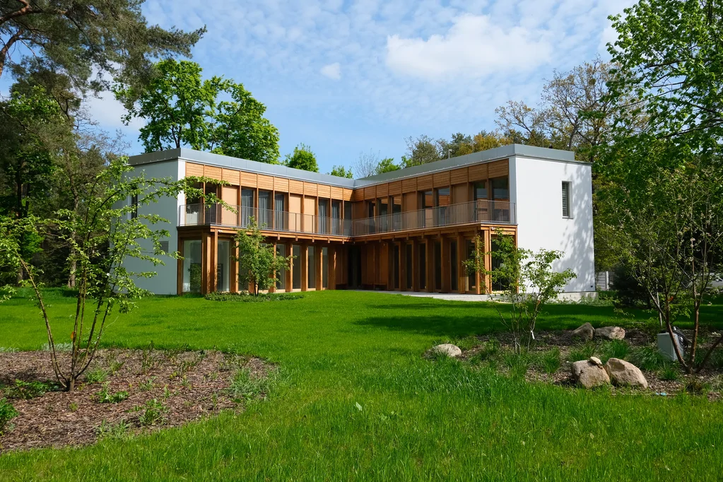 Szerokie ujęcie domu od strony ogrodu z drewnianą elewacją, balkonem i zadbanym trawnikiem z nasadzeniami