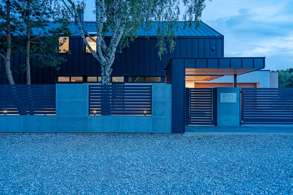 Front nowoczesnego domu wieczorem z grafitową elewacją i minimalistycznym ogrodzeniem.