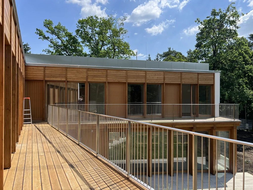 Taras na piętrze z metalową balustradą przy nowoczesnym budynku z drewnianą elewacją