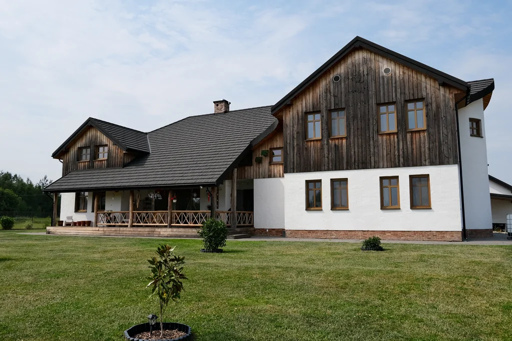 Widok z drona na boczną elewację z długą, zadaszoną werandą; obok widoczny sprzęt gospodarczy