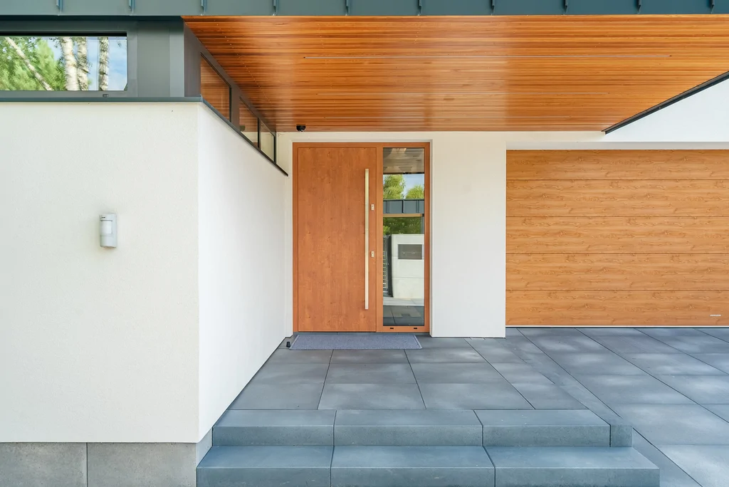 Zbliżenie wejścia do domu z drewnianymi drzwiami, drewnianą podsufitką i okładziną garażu.