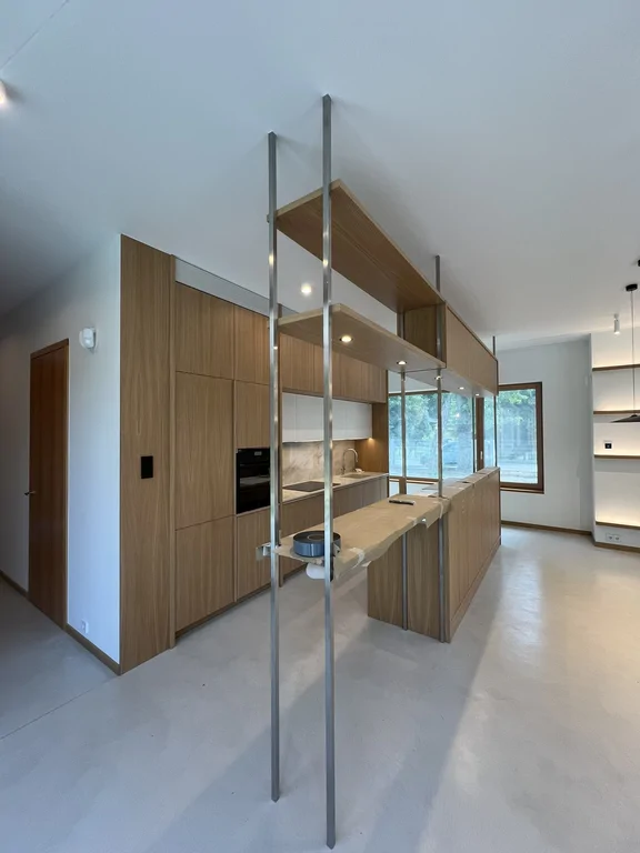 Kuchnia z wyspą, drewnianą zabudową i stalowym regałem w otwartej strefie dziennej