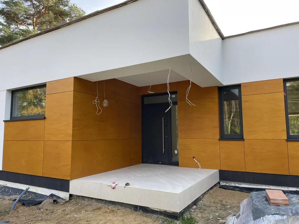 Wejście główne nowoczesnego domu z podcieniem, czarnymi drzwiami i elewacją w kolorze drewna