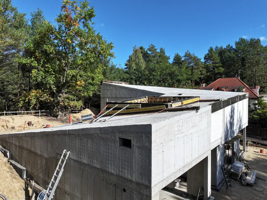 Zbliżenie z drona na narożnik żelbetowego budynku z pochyłym stropodachem i otworem technicznym w stropie.