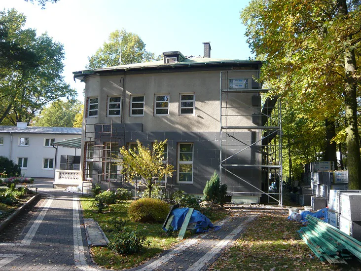 Budynek w trakcie remontu elewacji; rusztowania i prace przy ścianie od strony ogrodu.