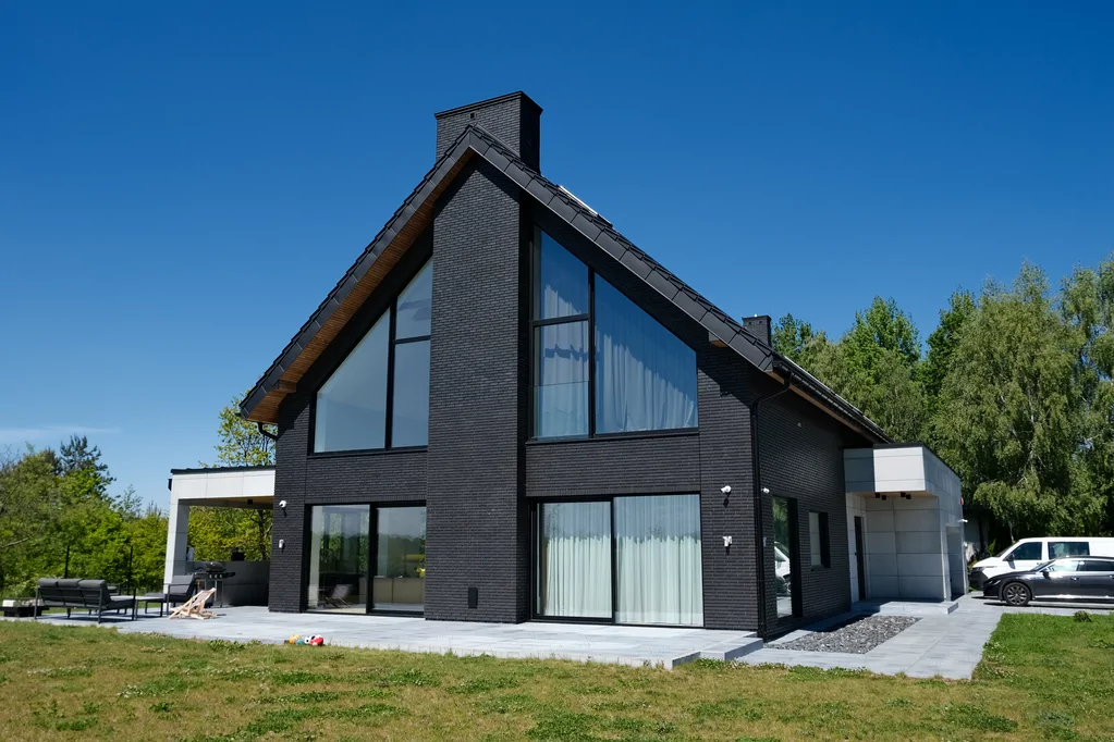 Elewacja ogrodowa domu w Ruścu: duże przeszklenia, taras oraz boczna bryła garażu z jasną okładziną.