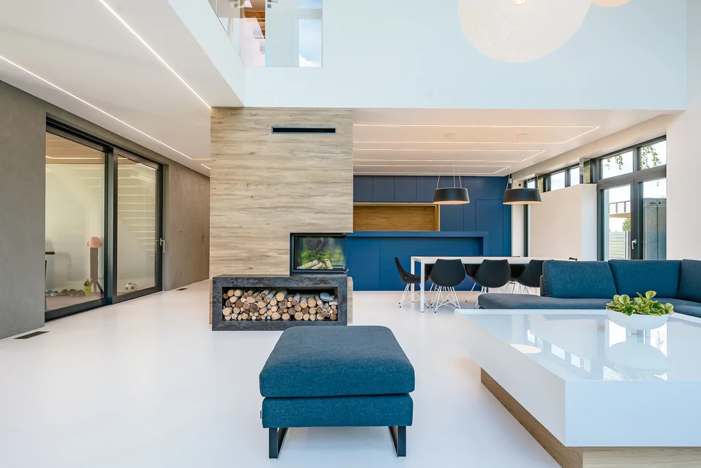 Szeroki widok salonu z kominkiem, jadalnią i granatową kuchnią w układzie open space.