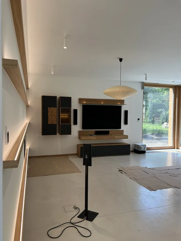 Strefa RTV w salonie z dużym telewizorem, drewnianą zabudową i wysokim przeszkleniem