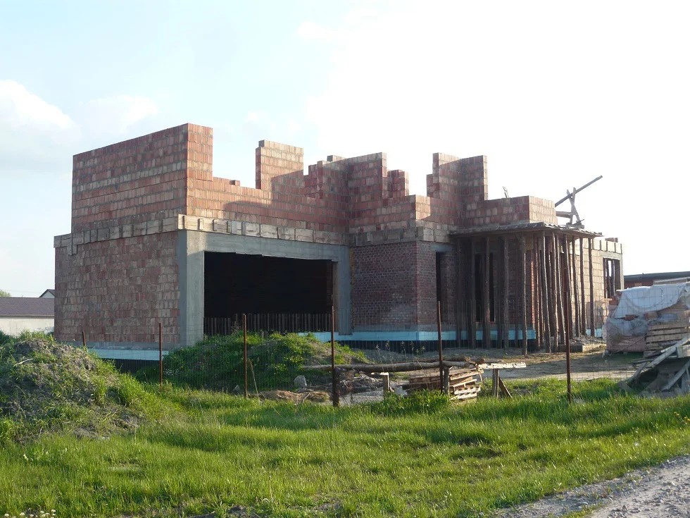 Stan surowy otwarty domu: wymurowane ściany i duży otwór garażowy, podparte szalunki