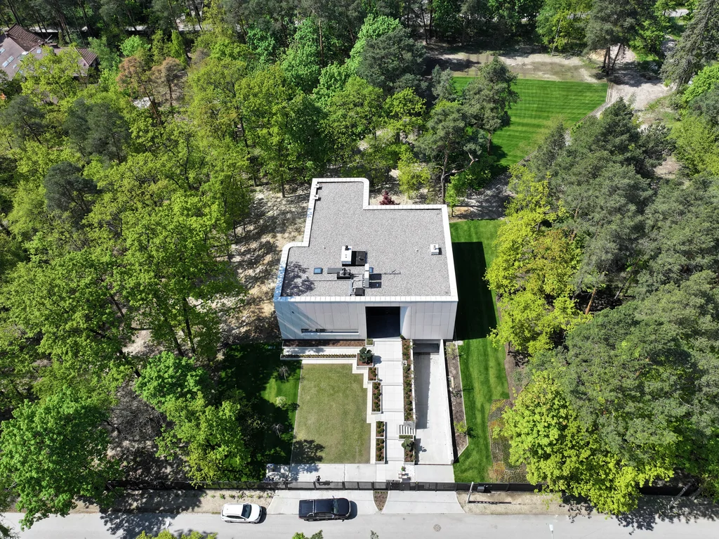 Wysokie ujęcie z lotu ptaka pokazujące nowoczesny dom na dużej leśnej działce z wyraźnym układem frontowego ogrodu