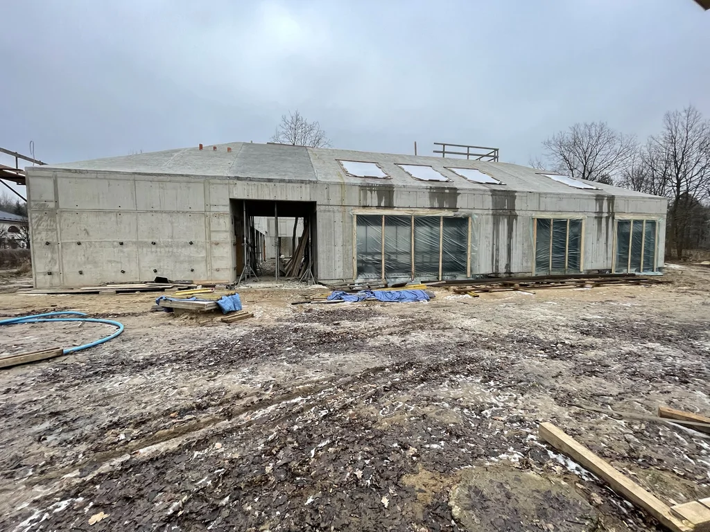 Elewacja w stanie surowym: beton architektoniczny oraz żelbetowy dach po skosie z otworami, stolarka zabezpieczona