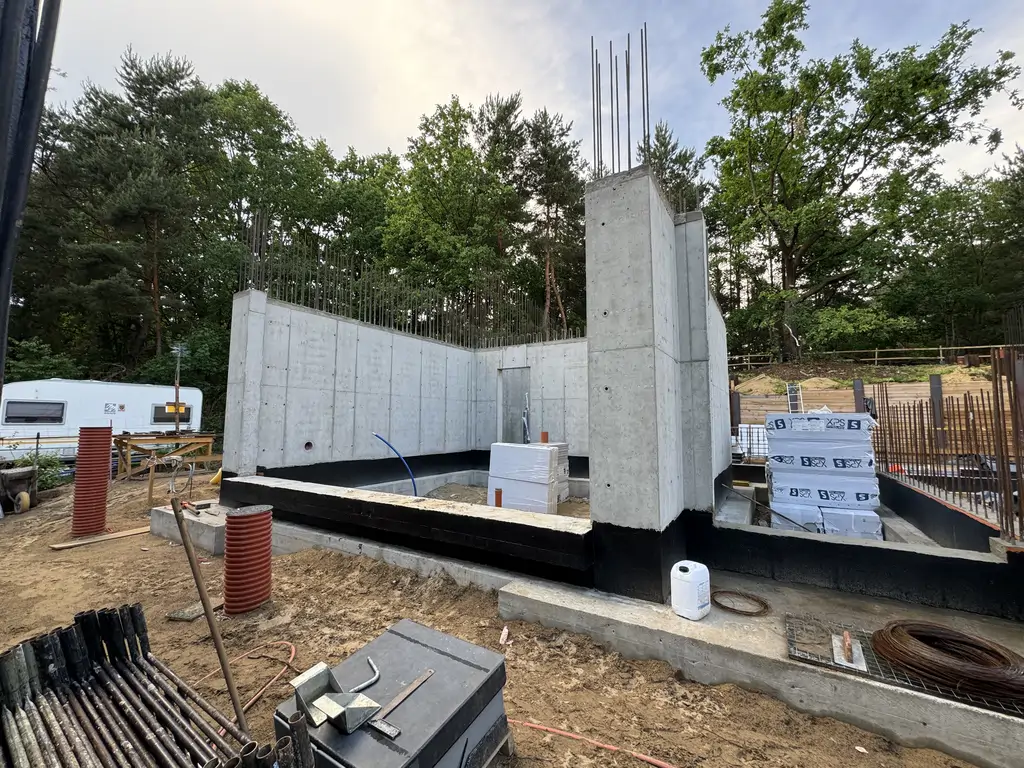 Żelbetowe ściany szczelnej piwnicy w trakcie realizacji z widoczną izolacją przeciwwodną.