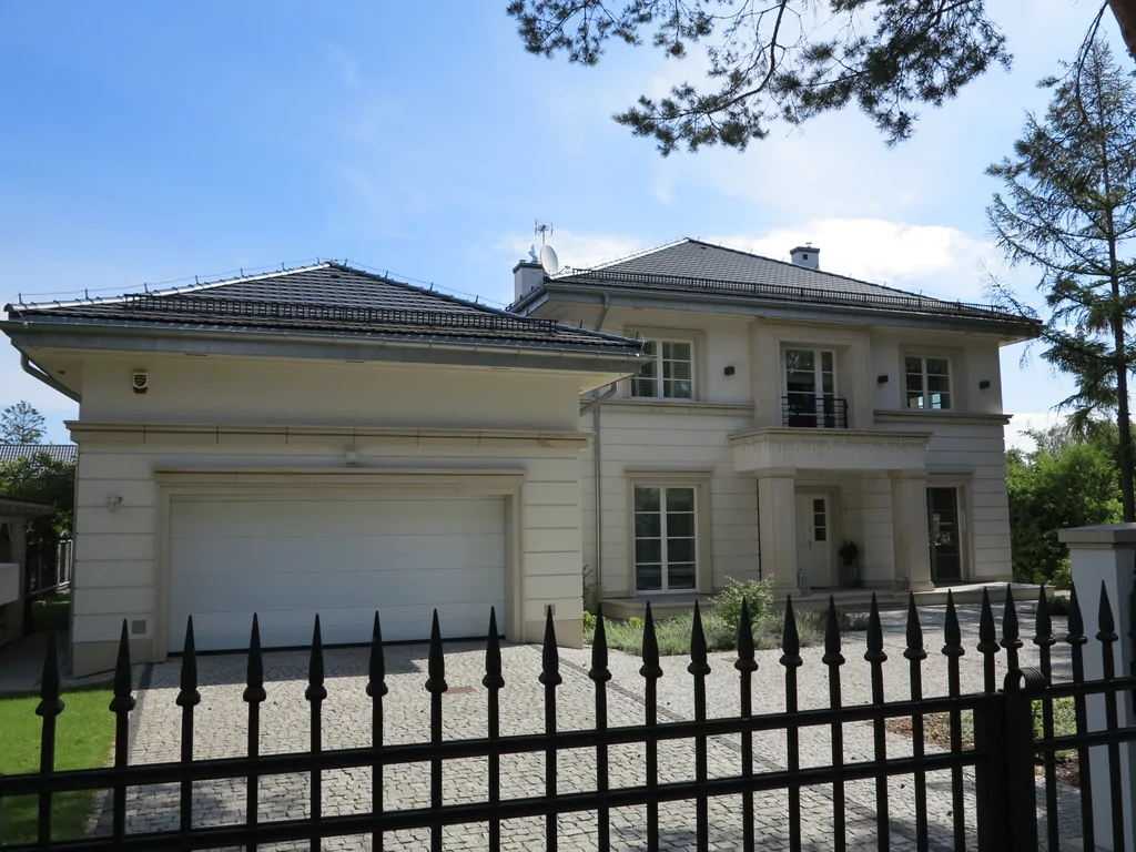 elewacja frontowa domu z garażem i wejściem, widok zza metalowego ogrodzenia