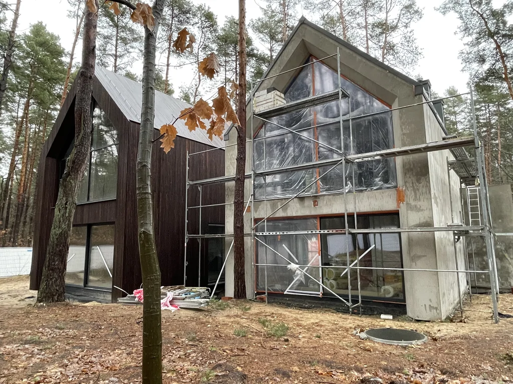 Dwie bryły nowoczesnego domu w trakcie prac elewacyjnych, jedna wykończona drewnem, druga przygotowana pod tynk