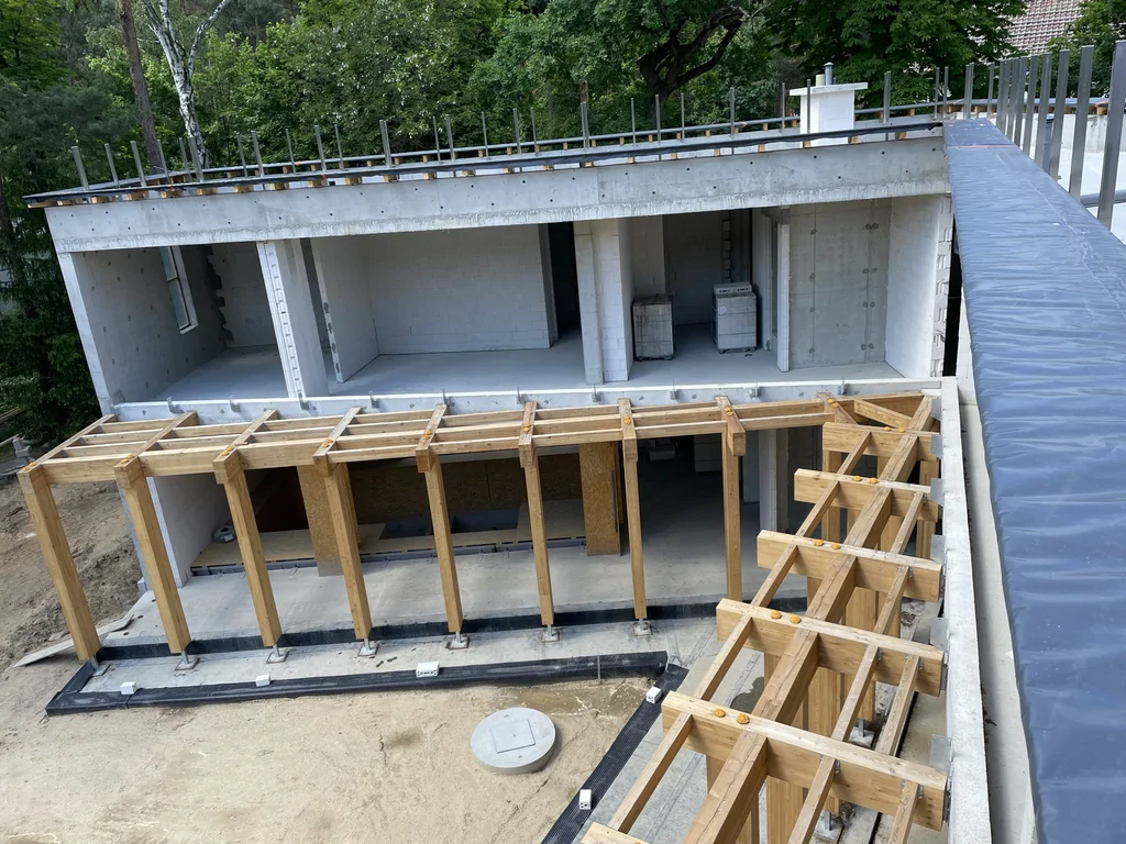 Widok z góry na drewnianą konstrukcję pergoli oraz wewnętrzny dziedziniec domu w stanie surowym