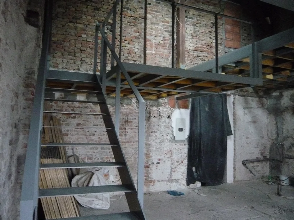 Montaż stalowych schodów i antresoli w surowym wnętrzu z cegły, konstrukcja stalowa z balustradą