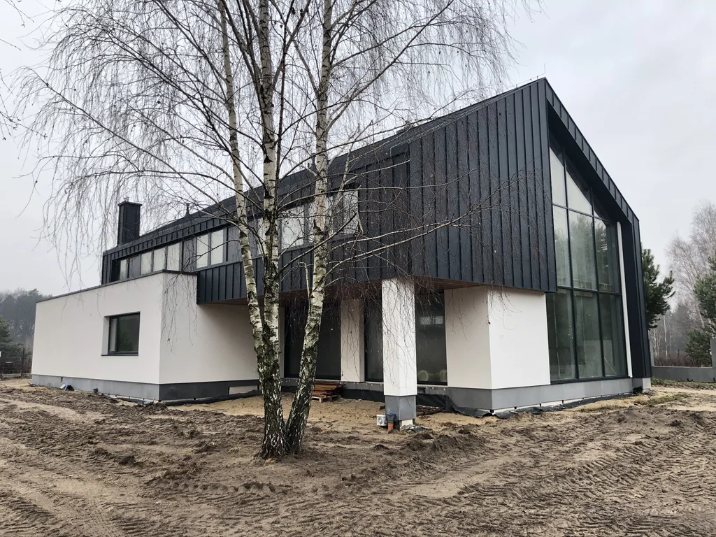 Nowoczesny dom w trakcie zagospodarowania terenu, widok narożny z brzozami
