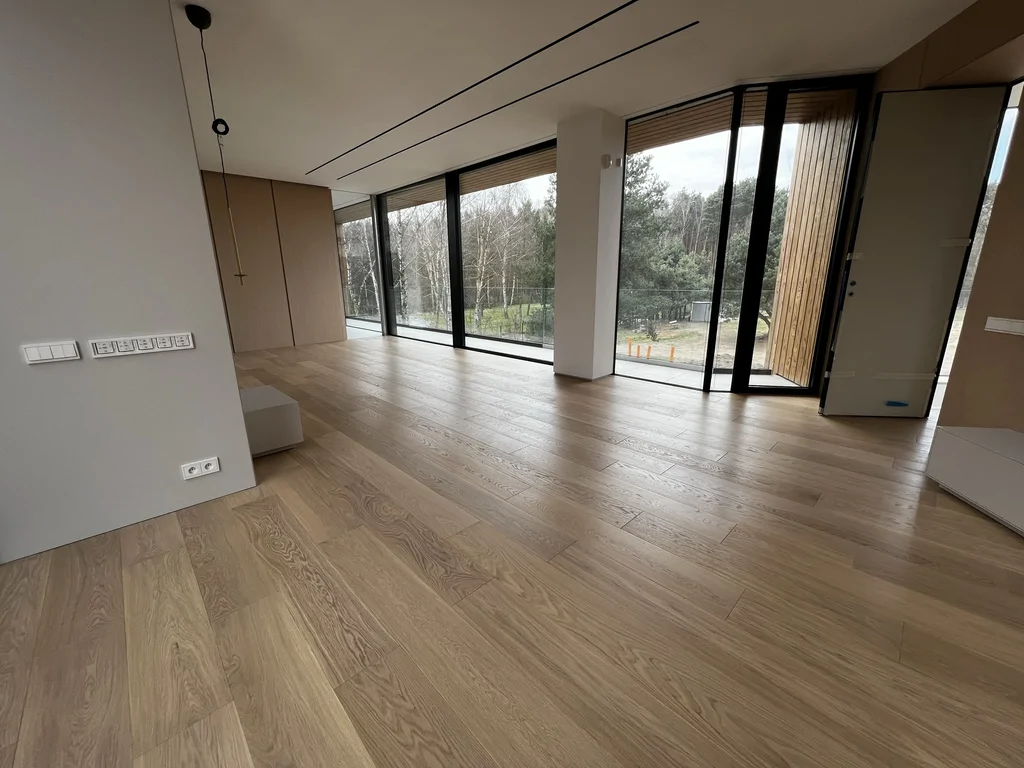 Komunikacja i część wypoczynkowa w jednej osi, z podkreśleniem długości przeszkleń oraz rytmu opraw sufitowych.