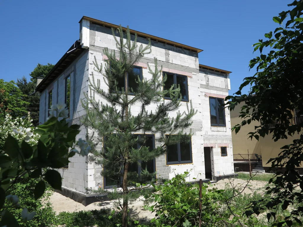 Widok na dom w stanie surowym zamkniętym ze stolarką okienną w ciemnym kolorze, mury wykonane z silikatów