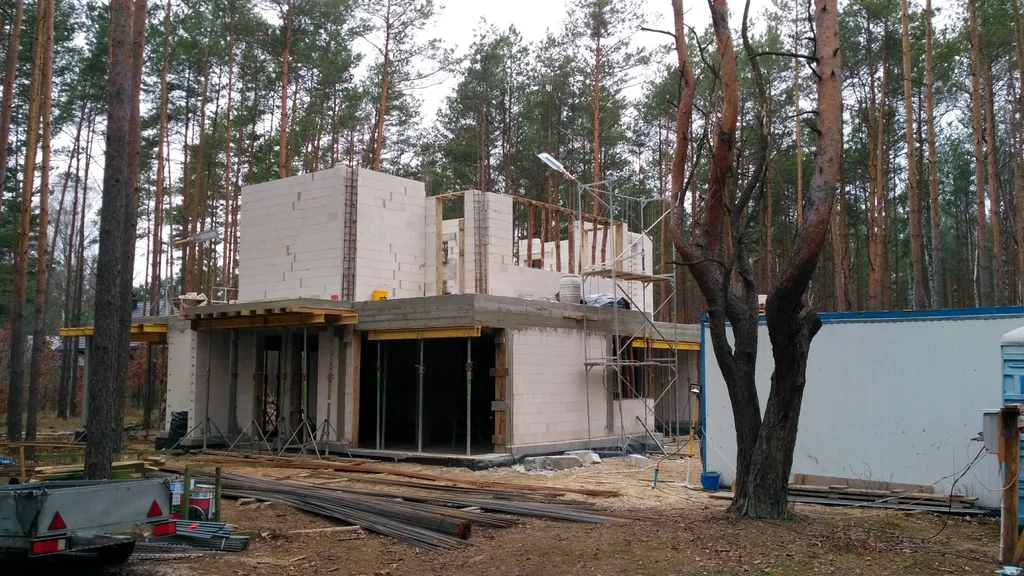 Stan surowy domu: ściany z bloczków i strop, rusztowanie oraz zaplecze budowy w lesie