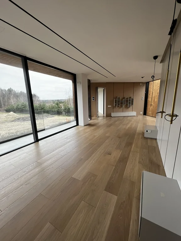 Szerokie przeszklenia oraz podłoga drewniana prowadzą optycznie przez całą przestrzeń. Oświetlenie liniowe w suficie.