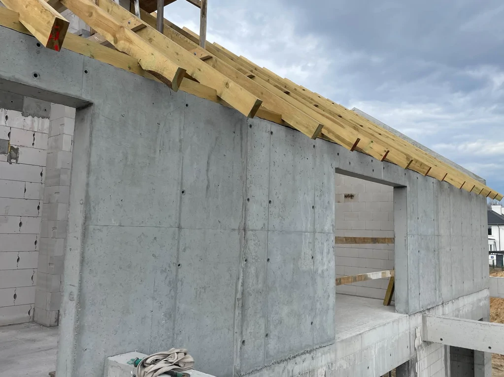 Żelbetowa ściana zewnętrzna z przygotowaną konstrukcją dachu oraz otworami pod stolarkę w stanie surowym