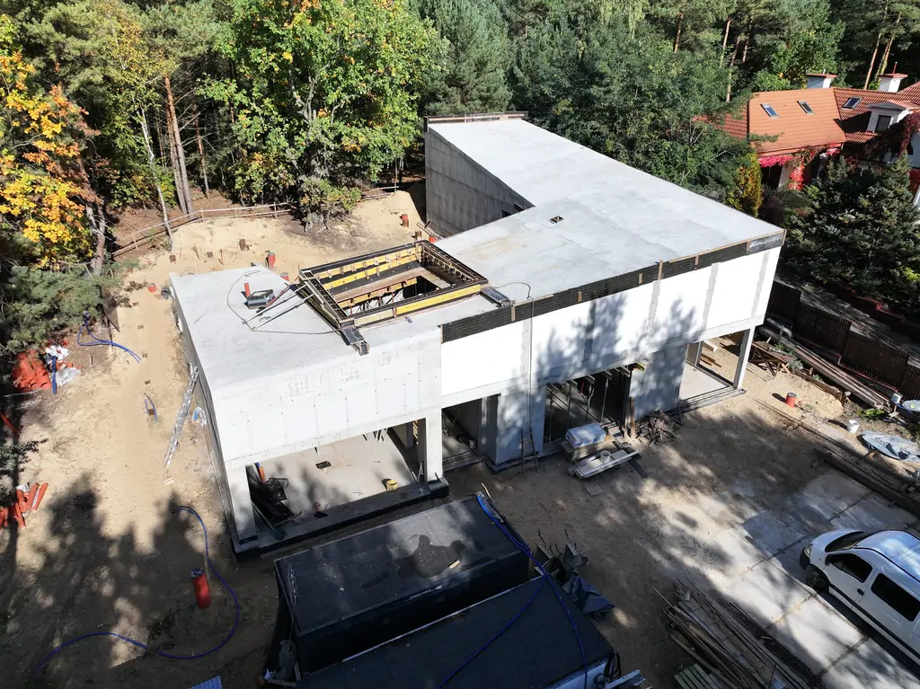 Widok z drona na front nowoczesnego domu w trakcie budowy z żelbetową konstrukcją i dużymi otworami okiennymi.