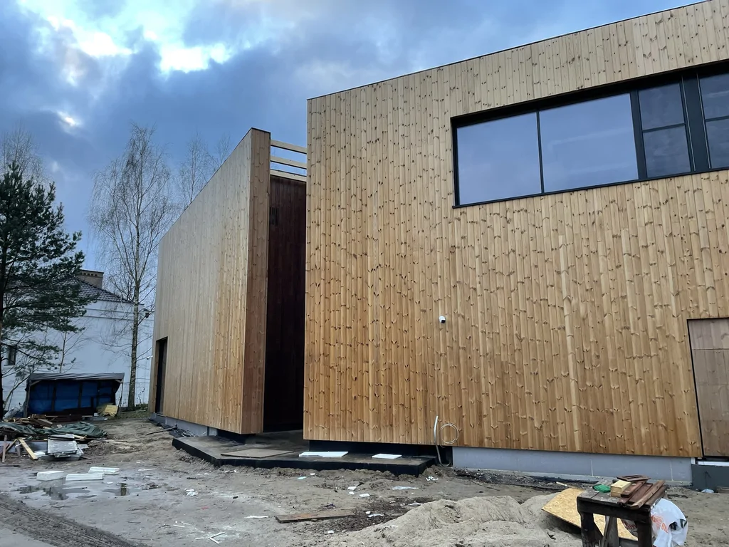 Dwie prostopadłościenne bryły domu z elewacją drewnianą; pomiędzy segmentami wąska strefa łącząca (atrium).