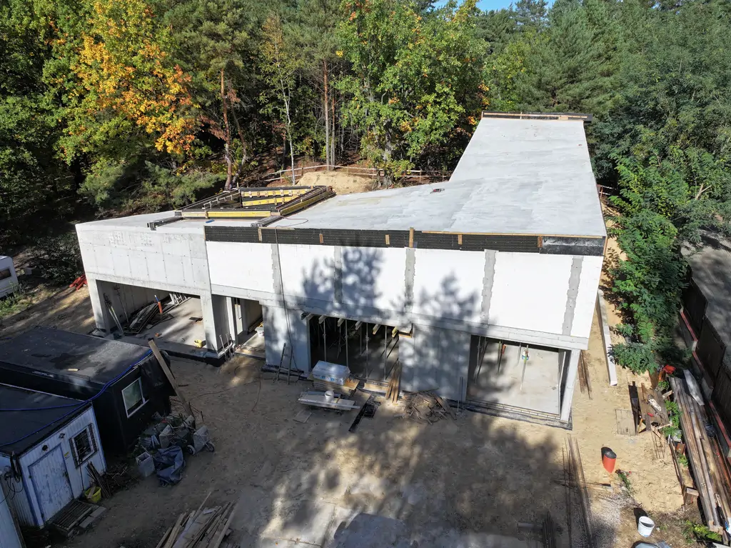 Ujęcie z drona pokazujące nowoczesny budynek żelbetowy z płaskim i pochyłym stropodachem oraz dziedzińcem wewnętrznym.