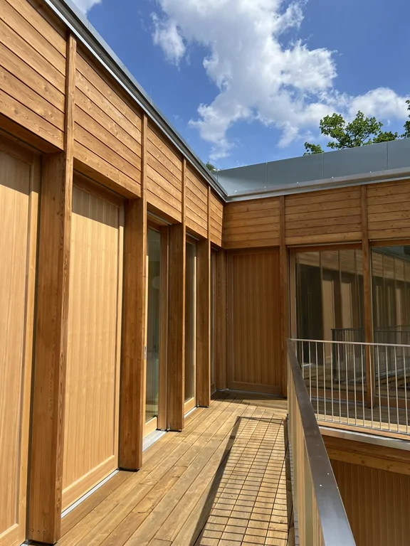 Narożny fragment tarasu w wewnętrznym dziedzińcu z drewnianą elewacją i metalową balustradą