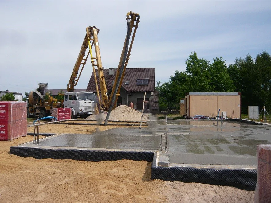 Wykonana posadzka na gruncie po wylaniu betonu, w tle pompa do betonu.