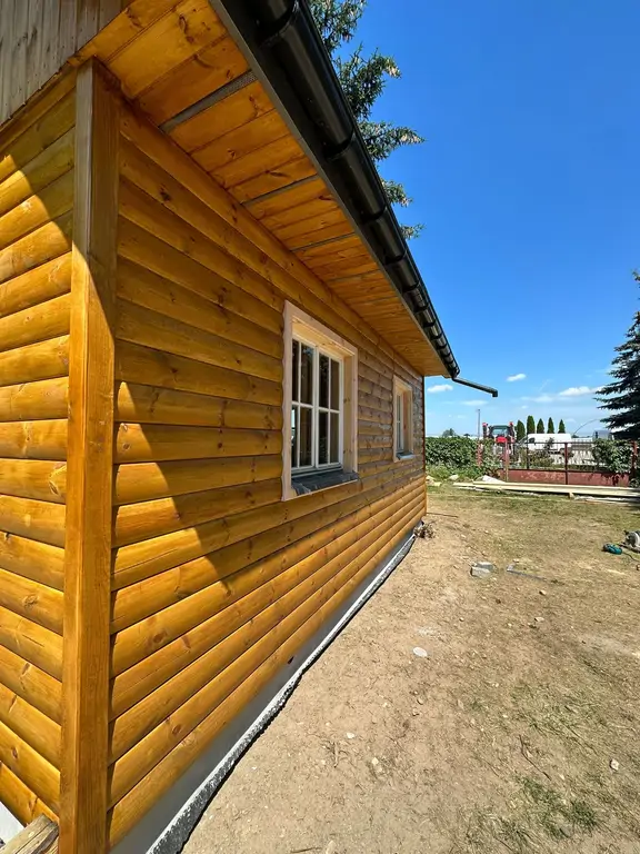 Domek drewniany po odnowieniu – widok z narożnika z nową elewacją i rynnami.