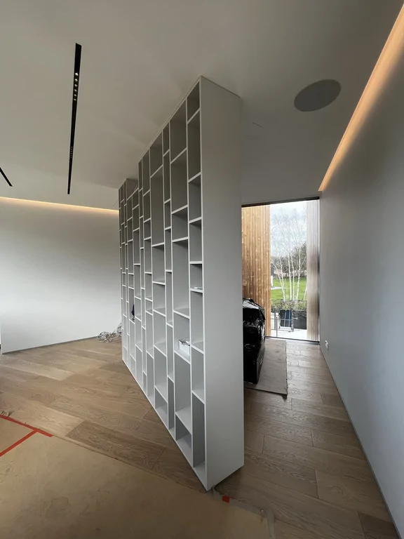 Wolnostojąca zabudowa regałowa jako lekka przegroda; porządkuje przestrzeń i nie zabiera światła.