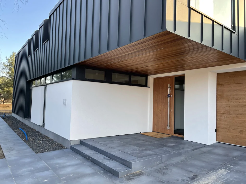 Wejście do nowoczesnego domu pod nadwieszoną bryłą, drewniany sufit i drzwi wejściowe