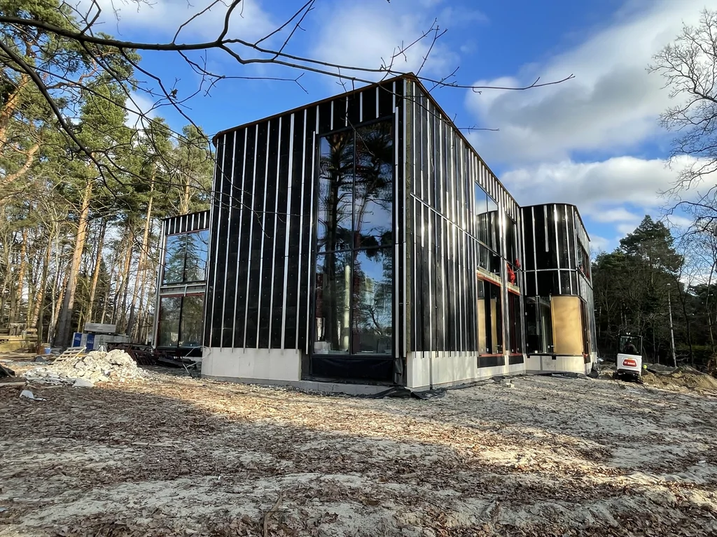 Szeroki widok nowoczesnego domu o geometrycznej bryle z ciemną elewacją i dużymi przeszkleniami