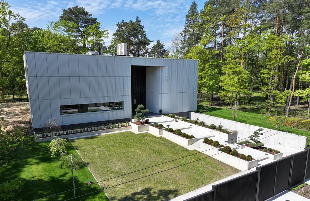 Szeroki widok z drona na front domu z geometrycznym układem schodów, donic i ogrodu wejściowego