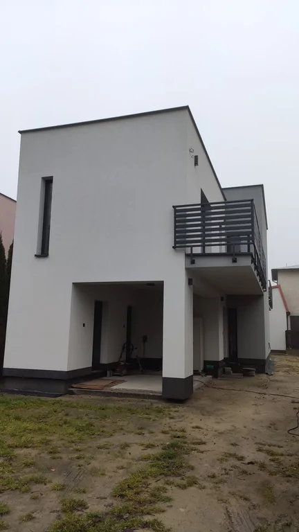 Budynek w stanie deweloperskim, dach płaski, jasna elewacja, barierki stalowe nad balkonem