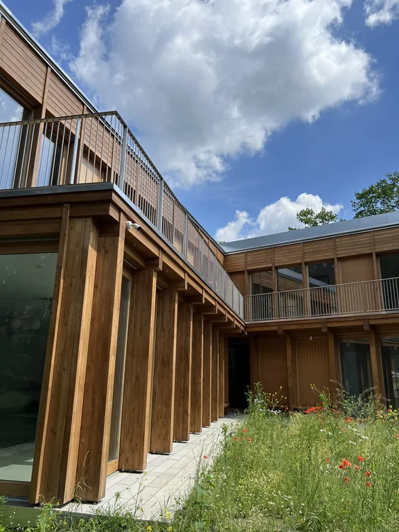 Widok na wewnętrzny dziedziniec z drewnianą elewacją, balkonami i łąką kwietną