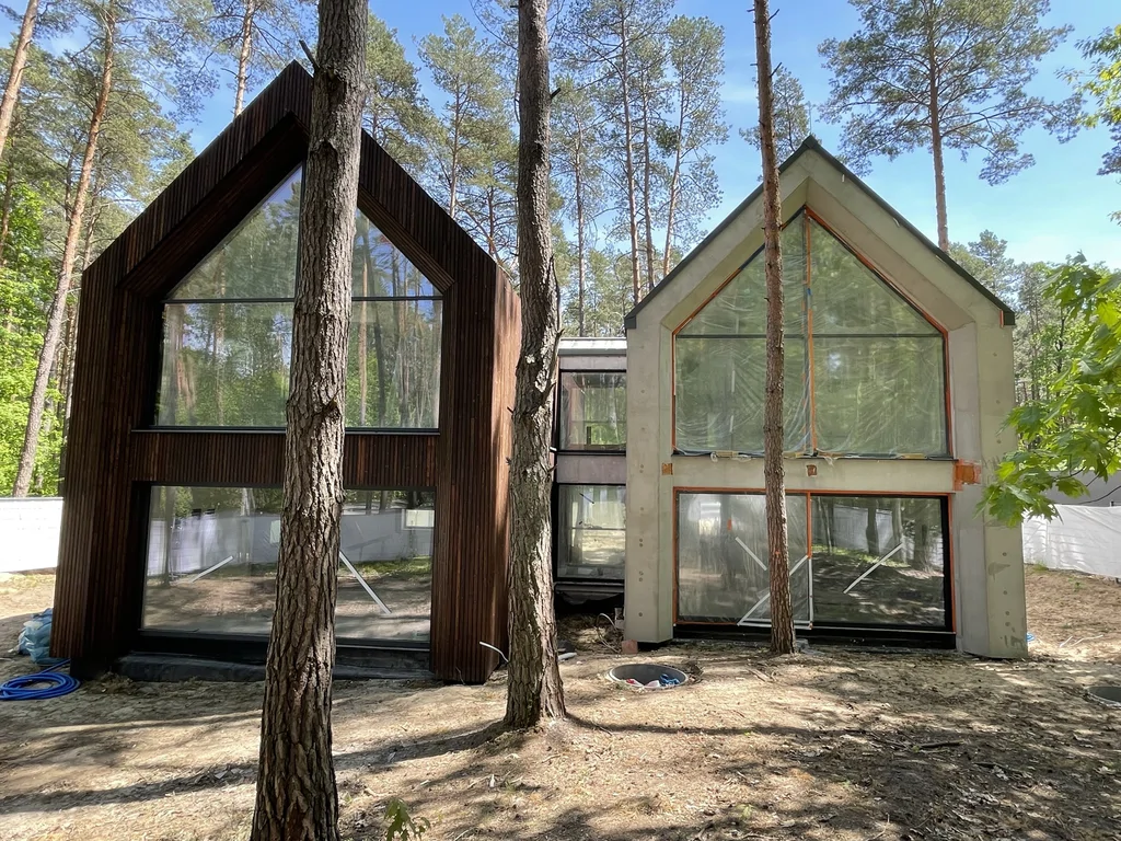 Front domu z dwiema wysokimi bryłami, dużymi przeszkleniami i elewacją częściowo wykończoną drewnem