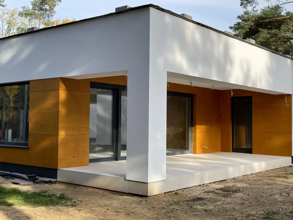 Narożnik tarasu nowoczesnego domu z białą bryłą, dużymi przeszkleniami i elewacją w kolorze drewna