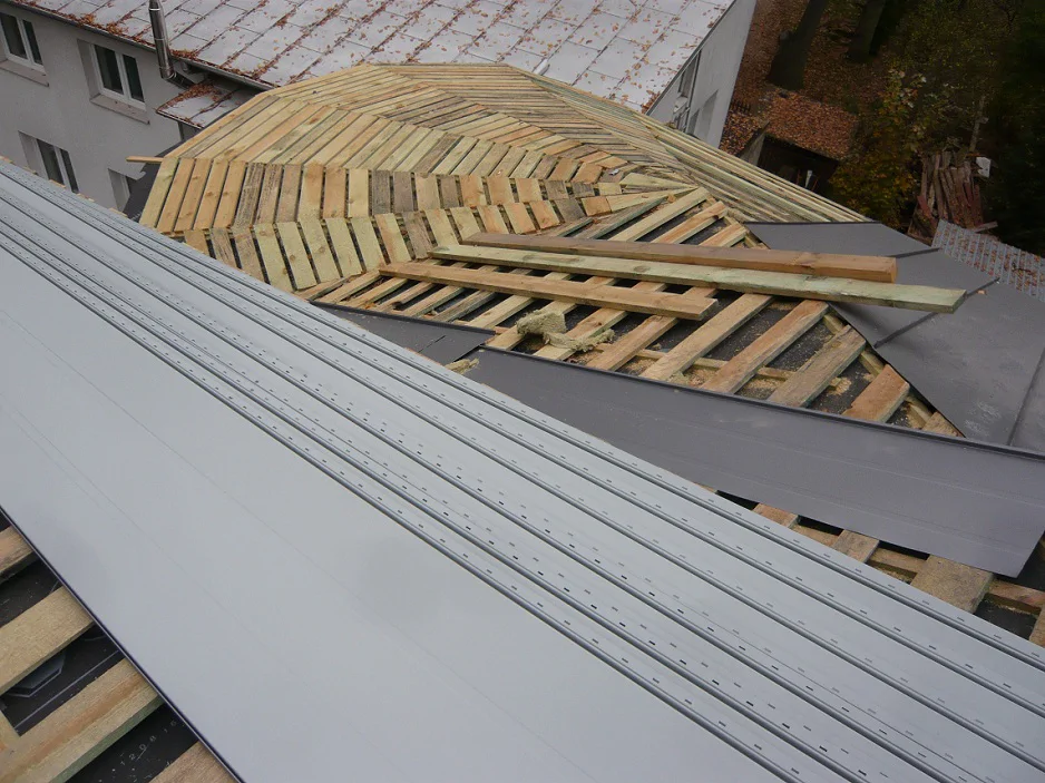 Montaż pokrycia dachu z blachy; układanie paneli obok zaokrąglonej części połaci.